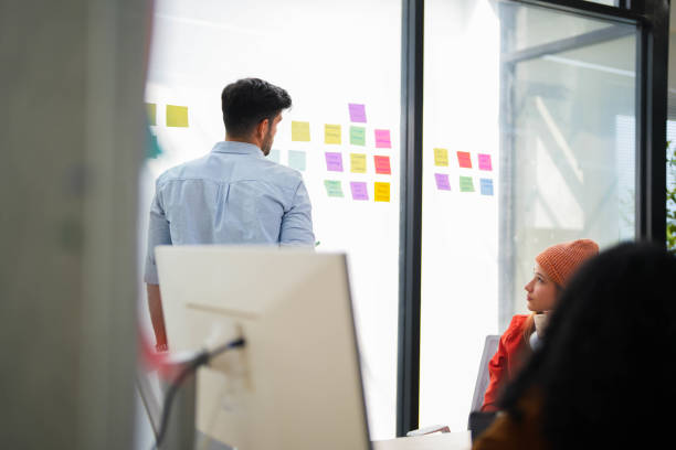 istock Confident male leader conducts a workshop, explaining ideas with sticky notes on a glass wall to colleagues. 2149597813
