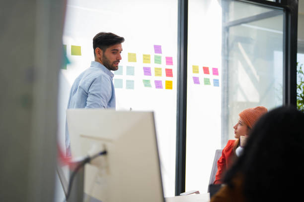 istock Confident male leader conducts a workshop, explaining ideas with sticky notes on a glass wall to colleagues. 2149598038