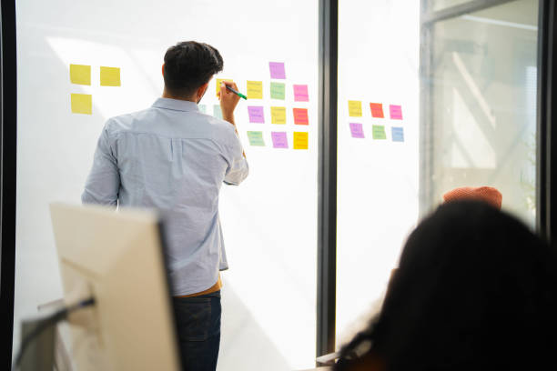 istock Confident male leader conducts a workshop, explaining ideas with sticky notes on a glass wall to colleagues. 2149598237