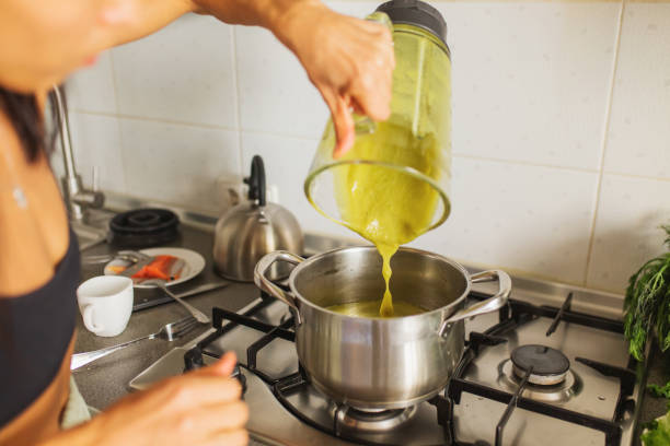 The preparation of a potato leek soup in a black cooking pot, a hand is stirring the soup with a wooden spoon