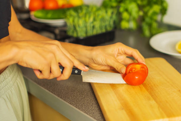 Woman cutting tomato on kitchen board.
