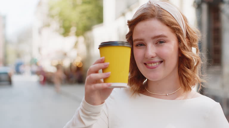 Happy redhead young smiling woman relaxing enjoying morning coffee hot drink outdoors city street