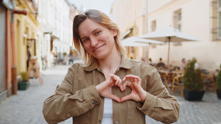 Woman makes symbol of love, showing heart sign to camera, express romantic feelings on city street