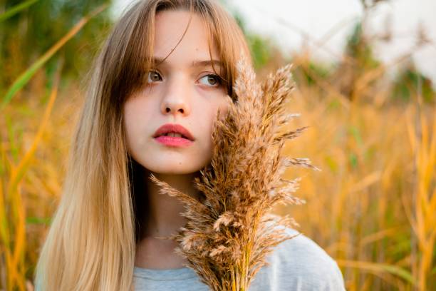 Beautiful young girl wearing blank gray t-shirt and black jeans posing against high green and yellow grass in early warm autumn. Outdoor portrait of beautiful female model.