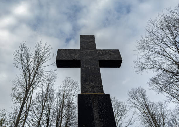 Religious cross over overcast sky with bare trees, gloomy mood, bottom view.