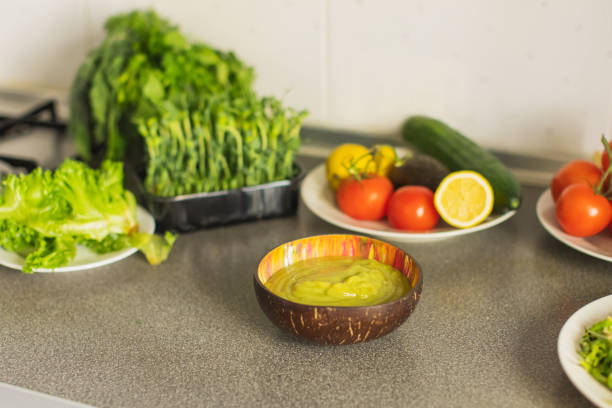 Close-up of a halved avocado with its seed intact next to a bowl of fresh cherry tomatoes on a wooden table. The natural sunlight enhances the colors and textures, highlighting the freshness of these nutrient-rich superfoods.