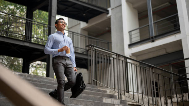 istock A confident businessman walks down stairs outside a building, holding a coffee cup and a briefcase. 2149605855