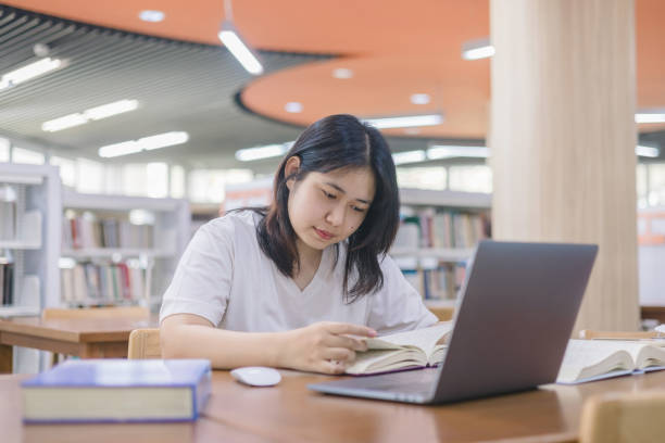 istock girl student study online with teacher, happy young woman with internet learning in library, distance education 2149608275