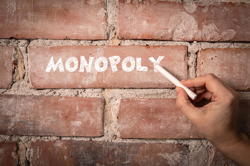 Monopoly. Text written with white chalk on a red brick background.