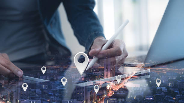 istock GPS map, pin address location on mobile apps. Double exposure of man hand using digital tablet searching target place on night cityscape while working on laptop computer. 2149611317
