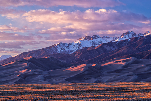Golden hour light warms up the peaks of the Sangre de Cristo Mountains and the tops of the sand dunes in Great Sand Dune National Park, Colorado