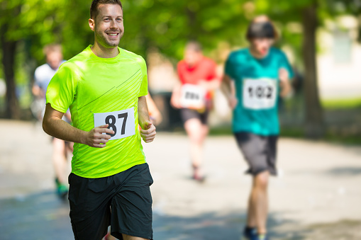 smiling man with start number running marathon on sunny day