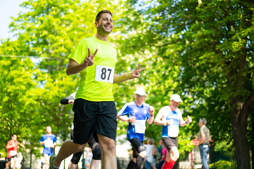 happy smiling man running marathon showing victory sign with fingers