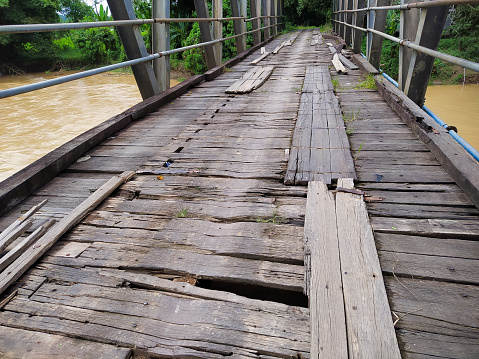 The wooden bridge is damaged and has holes that are dangerous to cross. Broken wooden bridge.