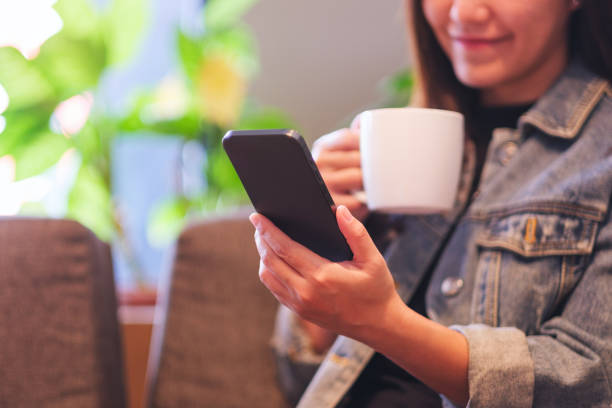 istock Closeup image of a young woman holding and using mobile phone while drinking coffee in cafe 2149613854