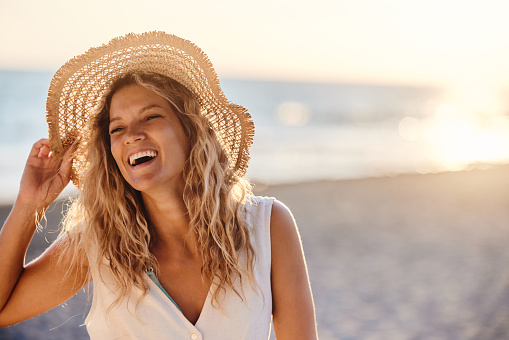 Young cheerful woman with sun hat having fun during summer day on the beach. Copy space.