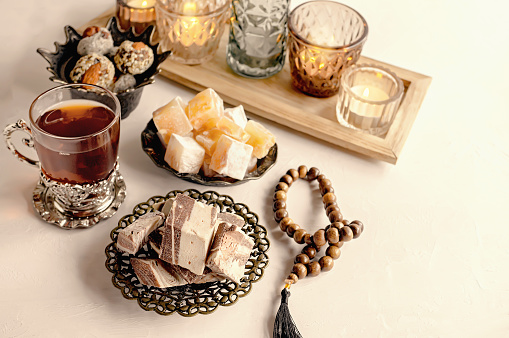 halva. Turkey glass of tea, candles, metal spoon and sunflower halva with almonds and pistachios stands on a light background.