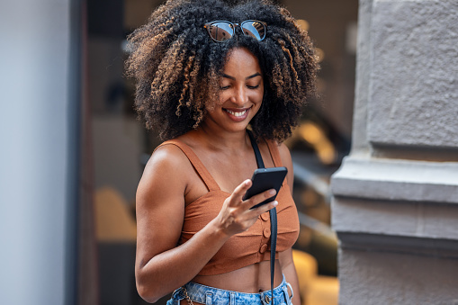 Close up of smiling woman using smartphone while carrying shopping bags walking through the city