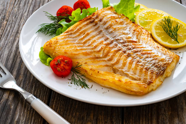 istock Fried cod fillet and fresh vegetables on wooden table 2149621293