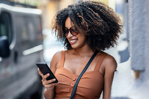 Close up of smiling woman using smartphone while carrying shopping bags walking through the city