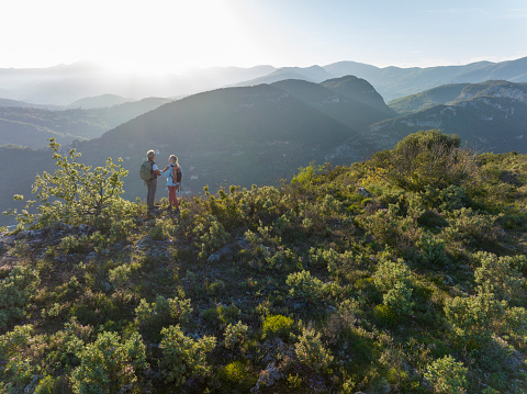 Aerial view of mature hiking couple watching sunset on top of hill,  Liguria