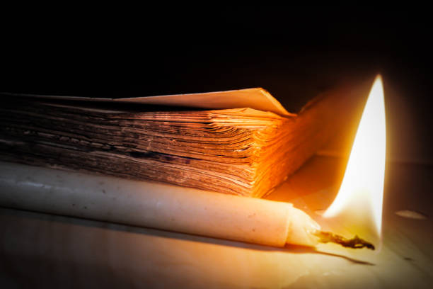 A thick book and a burning candle in a dark room