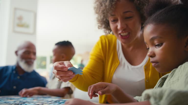 Grandparents With Grandchildren Indoors At Home Doing Jigsaw Puzzle With Parents In Background