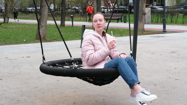 A young white girl drinking a cocktail, swinging on a swing, relaxing.