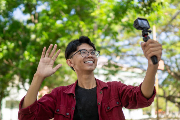 istock Asian man recording and talking to camera. Young man vlogging and taking selfie with action camera at public park. 2149625829