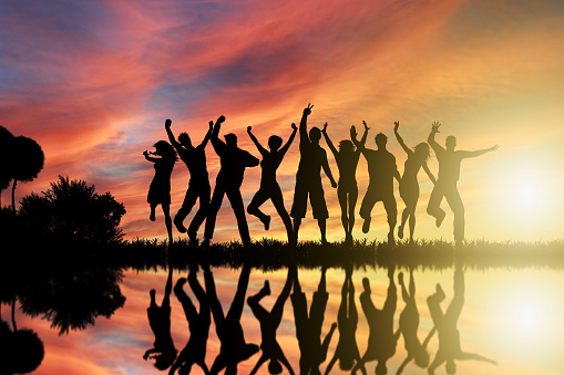 A group of friends captured in silhouette against a vivid sunset, reflecting on water, symbolizing joy and togetherness.