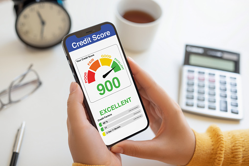 A person's hands holding a smartphone displaying a credit score of 900, indicating an excellent credit rating, with financial tools in the background.
