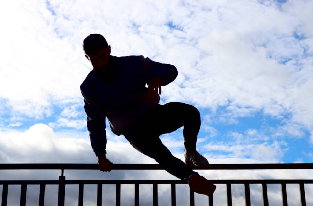 Silhouette of man jumping a fence, photo in mid-air, blue sky with clouds in the background