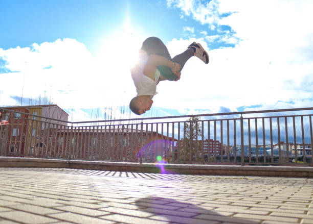 Caucasian man doing a flip in the city with sunlight and sky background, stands in the middle of the air