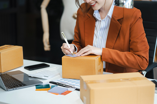 woman start up small business owner writing address on cardboard box at workplace.small business entrepreneur SME or freelance America woman working with box at home.