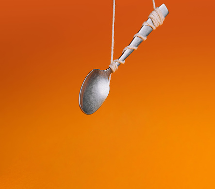 Silver spoon tied with string against a vibrant orange backdrop, creating an illusion of floating