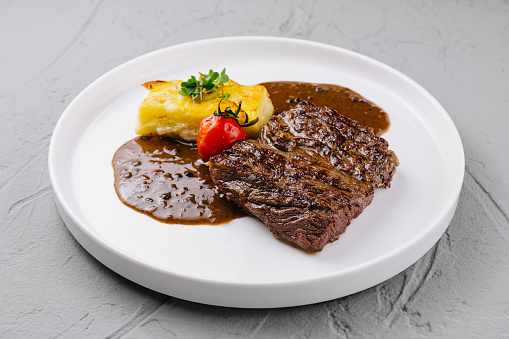 Juicy grilled beef steak served with a baked potato, fresh herb, and a rich brown sauce on a white plate