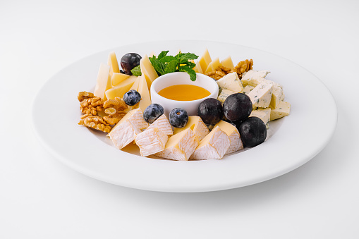 Elegant cheese plate with a variety of cheeses, walnuts, blueberries, and a bowl of honey, isolated on white