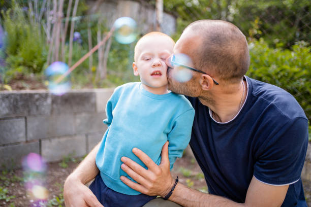 Happy father and his little son playing with soap bubbles. They are enjoying a hug and kissing.