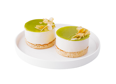 Two individual lime cheesecakes with almond slices on a white plate, isolated on white background
