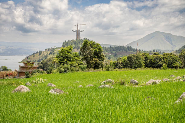 Samosir area, Lake Toba, North Sumatra, Indonesia - January 31th 2024:  Giant statue of Jesus Christ under construction with a lush rice paddy field in front