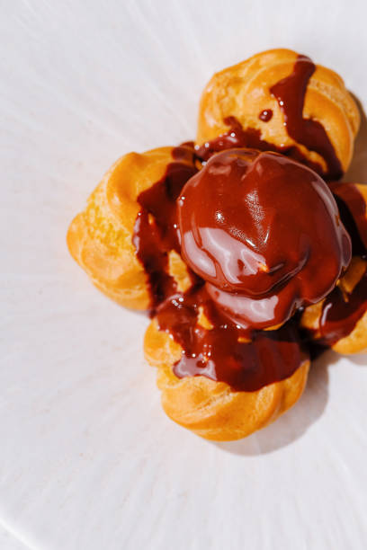 Indulgent french pastry profiteroles with decadent chocolate drizzle, baked to perfection and served as a luxurious dessert on a white background