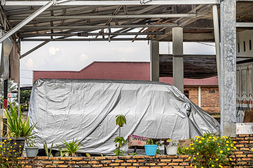 Samosir Island, Lake Toba, North Sumatra, Indonesia - February 1st 2024:  Car under a tarpaulin in front of a residential house in tropical surroundings