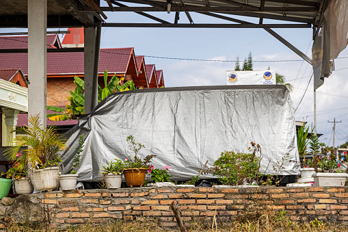 Samosir Island, Lake Toba, North Sumatra, Indonesia - February 1st 2024:  Car under a tarpaulin in front of a residential house in tropical surroundings