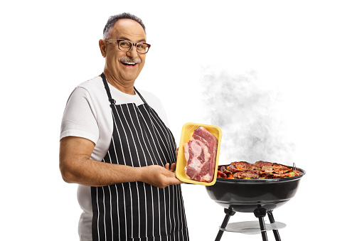 Man holding holding a pack of raw steak in front of a barbeque isolated on white background