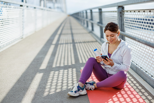 Flexibility in her fitness routine allows a mid-adult woman to use her mobile phone during a workout pause outdoors, demonstrating how modern technology supports her active lifestyle