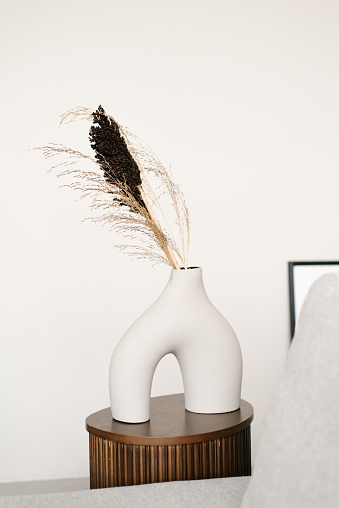 Stylish modern white ceramic vase interestingly shaped white ceramic vase with dried flowers in the decker of a Scandinavian living room or bedroom room