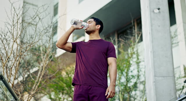 Man, fitness and drinking water in city for sports break, energy and workout performance. Thirsty athlete, asian runner and bottle for hydration, nutrition and healthy recovery for exercise outdoor