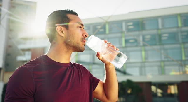 Man, drinking water and training in city for exercise break and health, energy or fitness goals in lens flare. Young thirsty athlete or runner thinking of his progress and bottle for outdoor workout