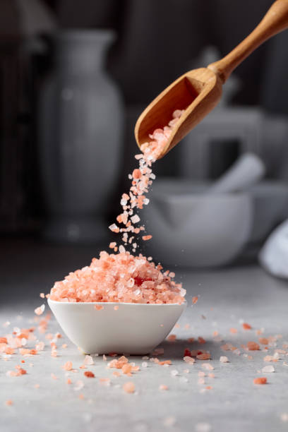 Pink salt in crystals is poured into a small white bowl.