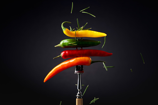 Colorful hot chili peppers sprinkled with rosemary on a black background. Concept of spicy food.